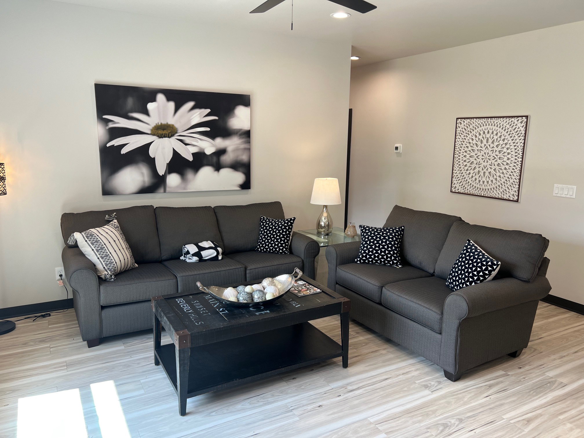 Spacious living area featuring light-toned walls, wood-finish flooring, and a ceiling fan