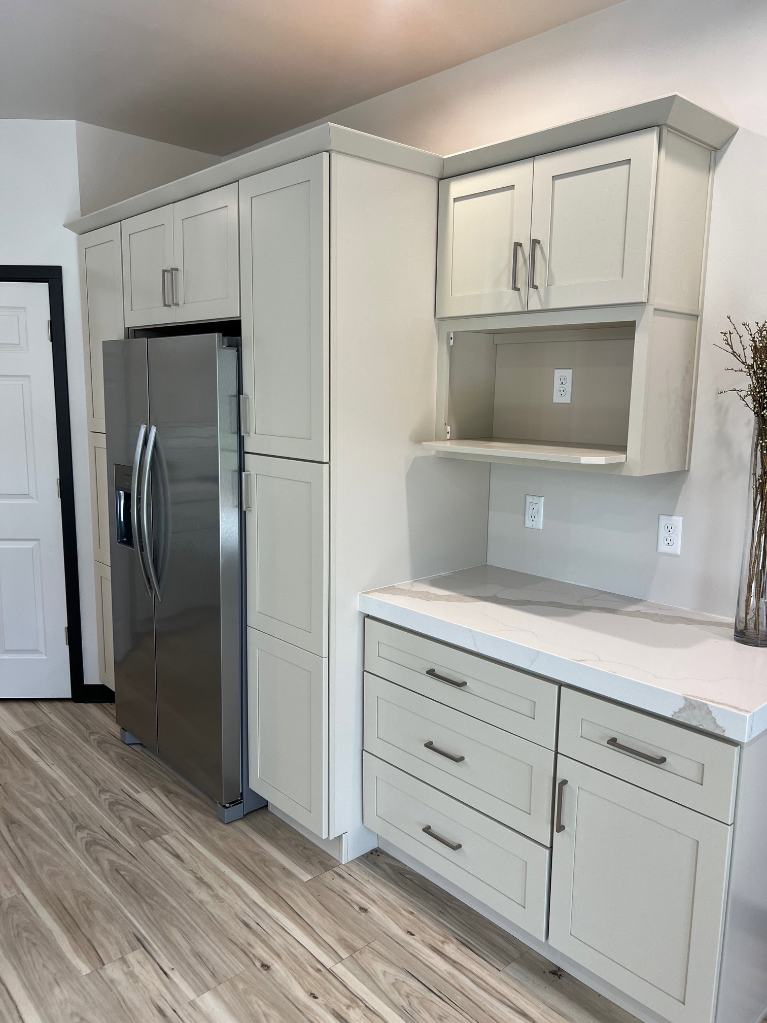 Kitchen featuring light-toned cabinetry with dark hardware, a built-in stainless steel refrigerator, and wood-finish flooring