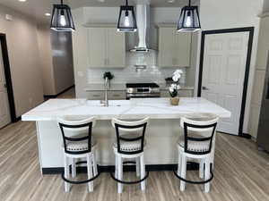 Kitchen featuring a large central island with a built-in sink, light-colored cabinetry, stainless steel appliances, a subway tile backsplash, and wood-finish flooring