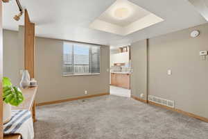 Spare room with light carpet, a tray ceiling, and a smoke detector