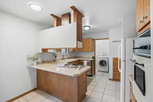 Kitchen with light countertops, a peninsula, light tile patterned flooring, wood finish cabinetry, and stainless steel appliances