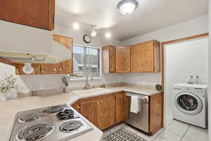 Kitchen with stainless steel appliances, washer / clothes dryer, light countertops, light tile patterned flooring, and wood finish cabinets