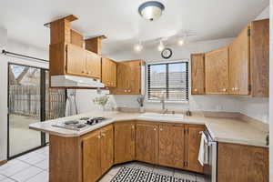 Kitchen featuring light countertops, light tile patterned floors, a peninsula, stainless steel electric stovetop, and track lighting