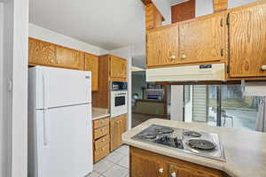 Kitchen featuring white appliances, light countertops, wood finish cabinetry, and light tile patterned flooring