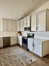 Kitchen featuring stainless steel appliances, dark wood-style flooring, light stone countertops, a textured ceiling, and decorative backsplash