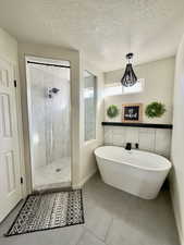 Bathroom with a shower stall, a freestanding tub, a textured ceiling, and tile patterned flooring