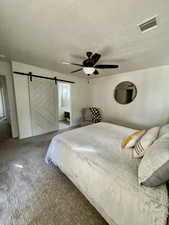 Carpeted bedroom with a barn door, a textured ceiling, and ceiling fan