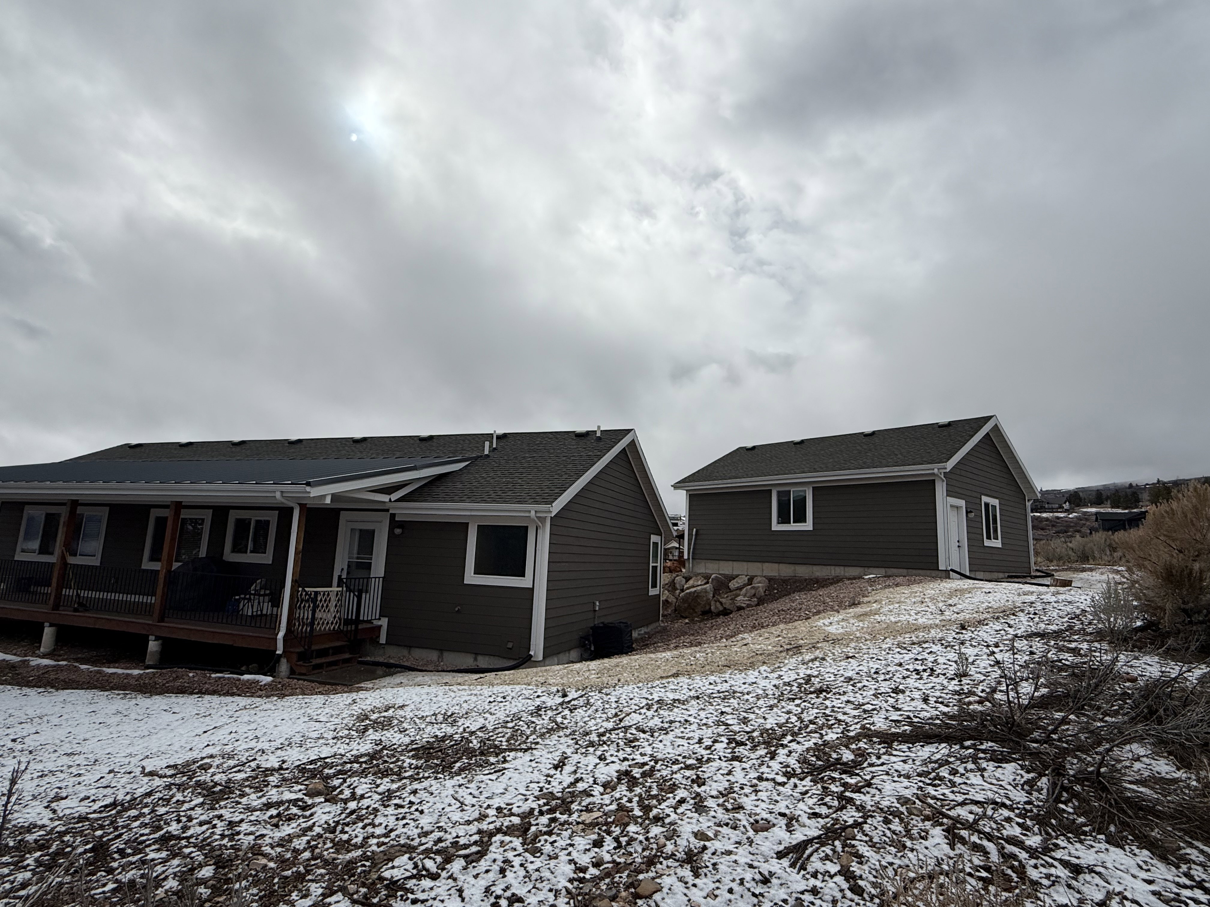 Snow covered rear of property with a wooden deck and a shingled roof