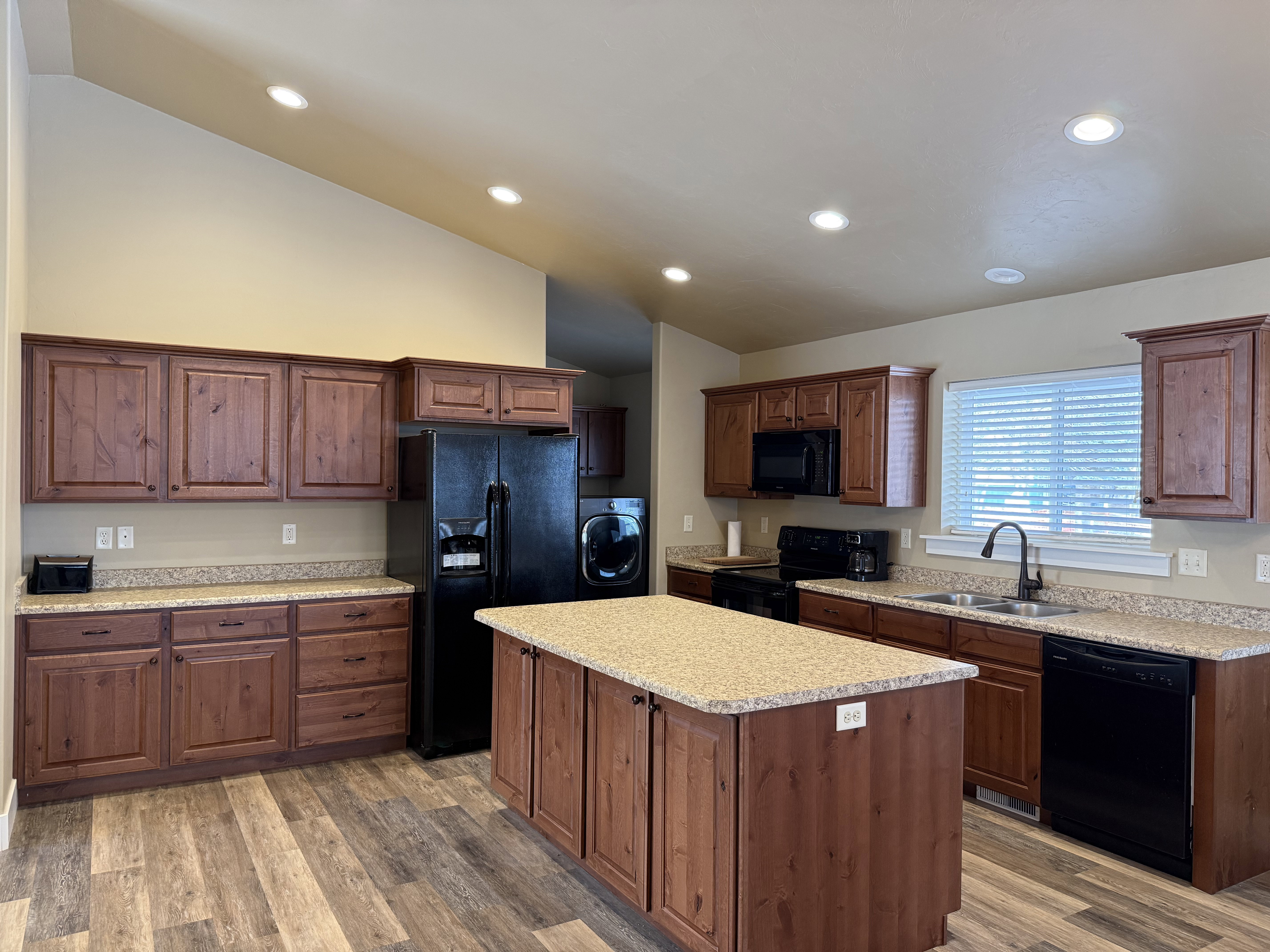 Kitchen featuring black appliances, washer / dryer, lofted ceiling, dark wood-type flooring, and a kitchen island
