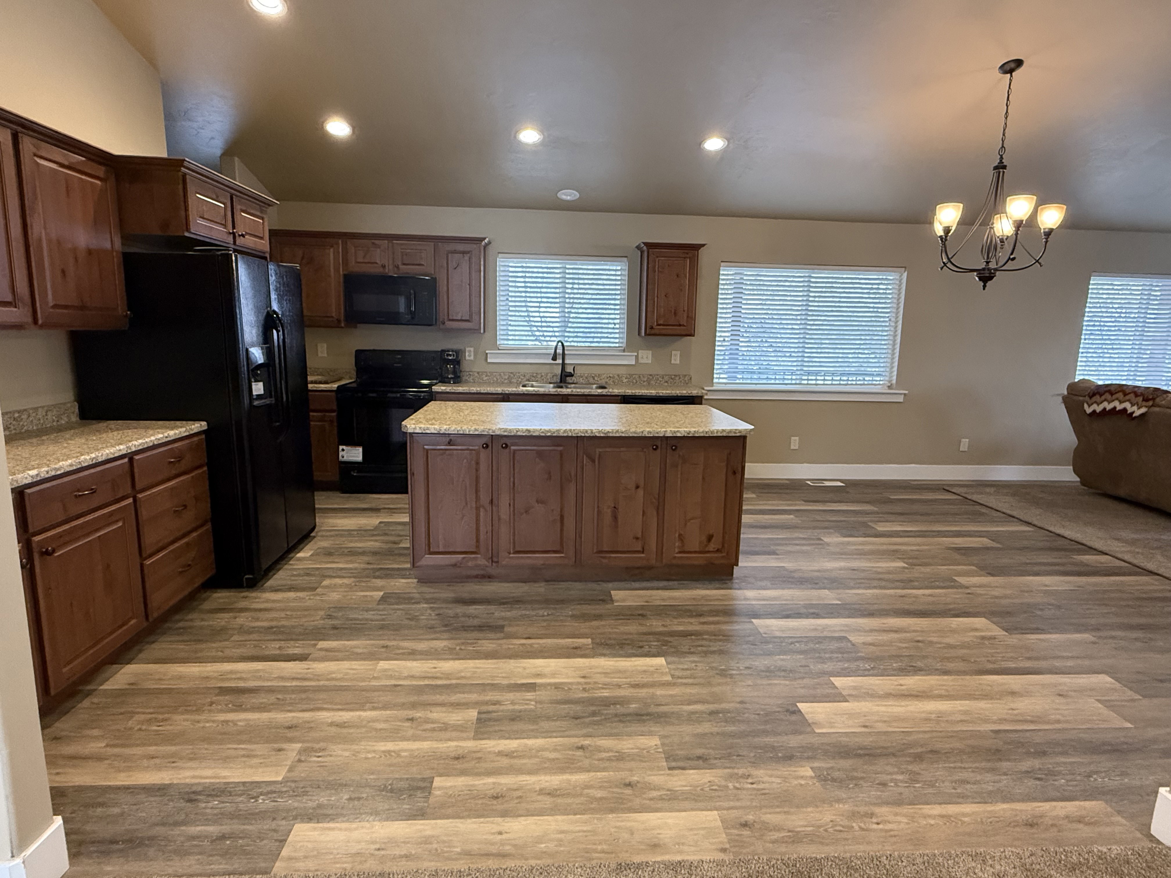 Kitchen with vaulted ceiling, black appliances, a chandelier, a kitchen island, and dark wood-type flooring