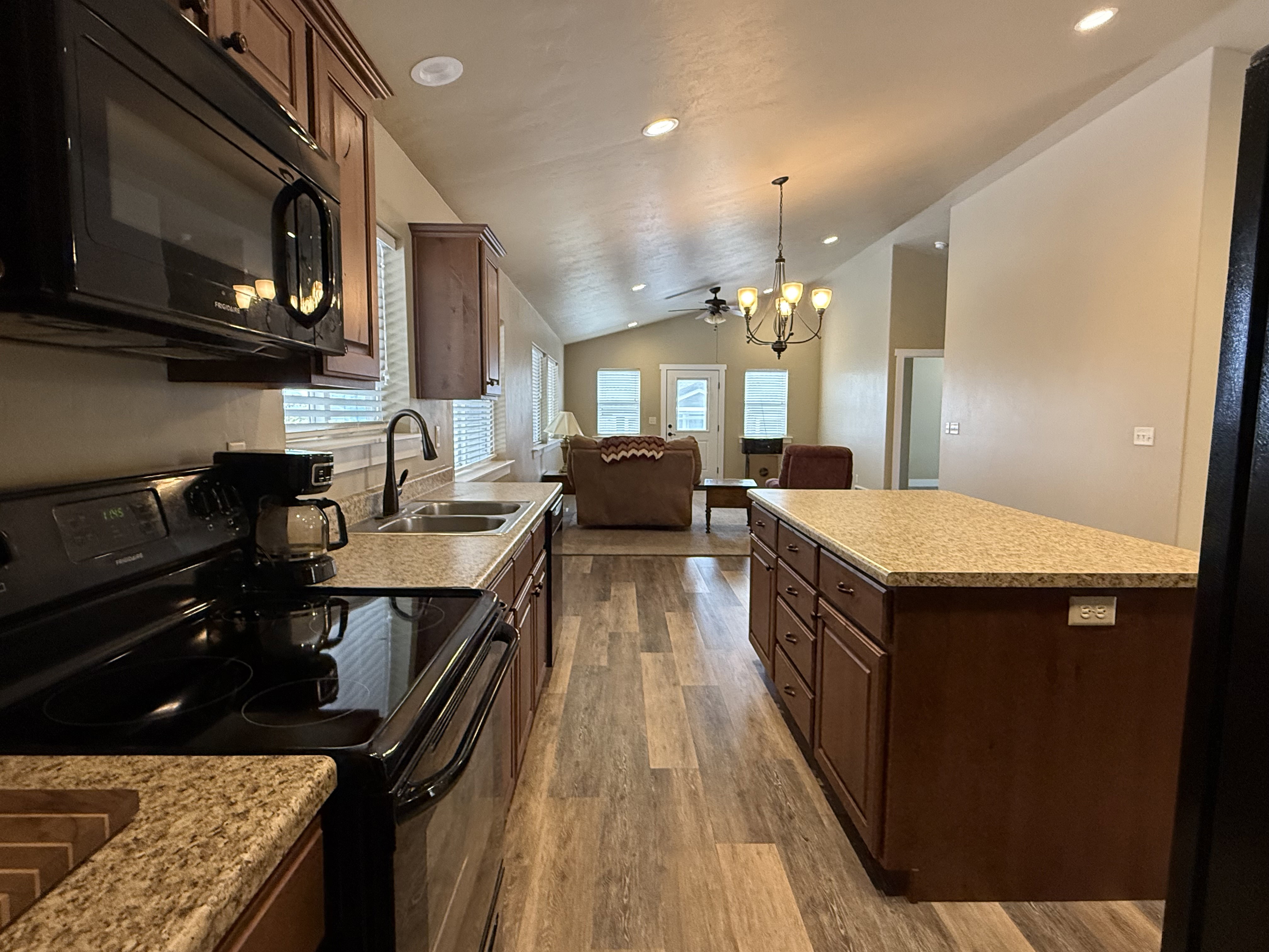 Kitchen featuring black appliances, vaulted ceiling, open floor plan, dark wood-type flooring, and a chandelier