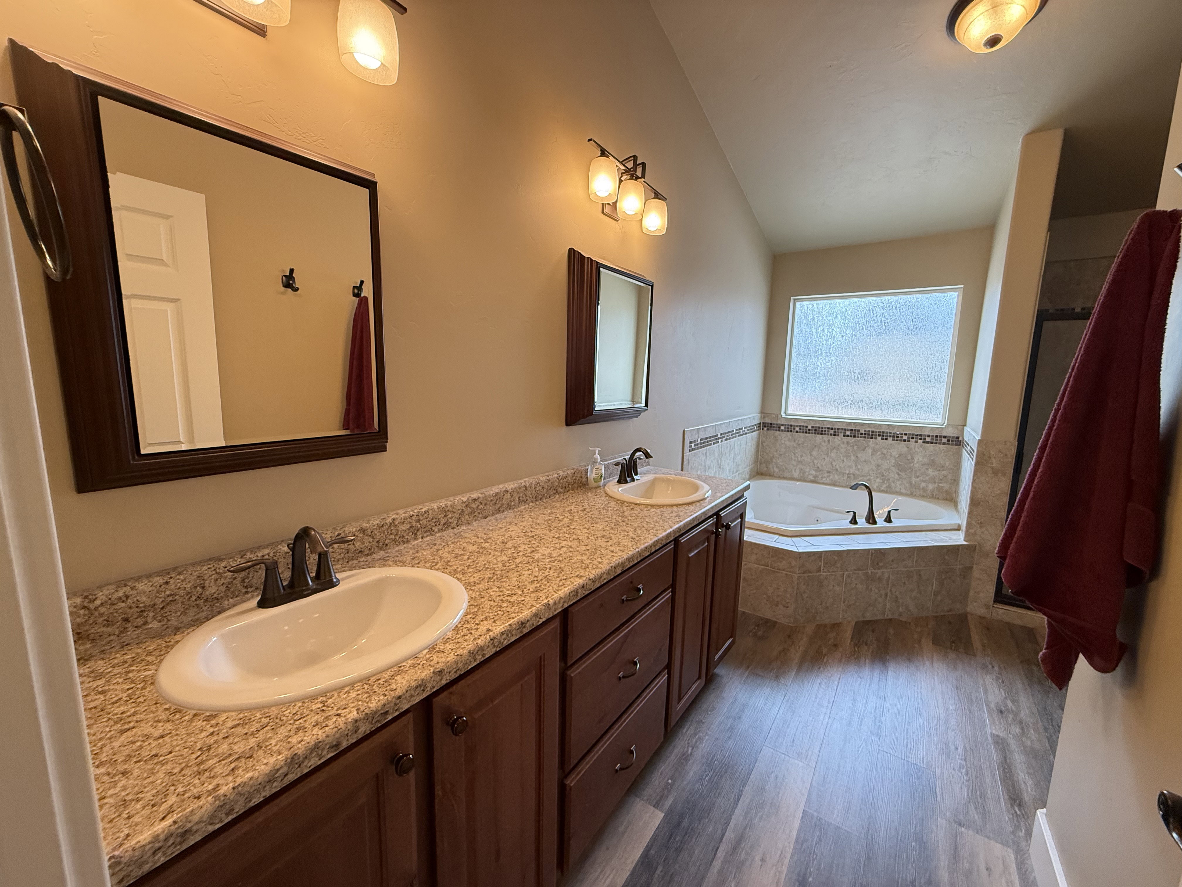 Full bath featuring double vanity, dark wood finished floors, a garden tub, and vaulted ceiling