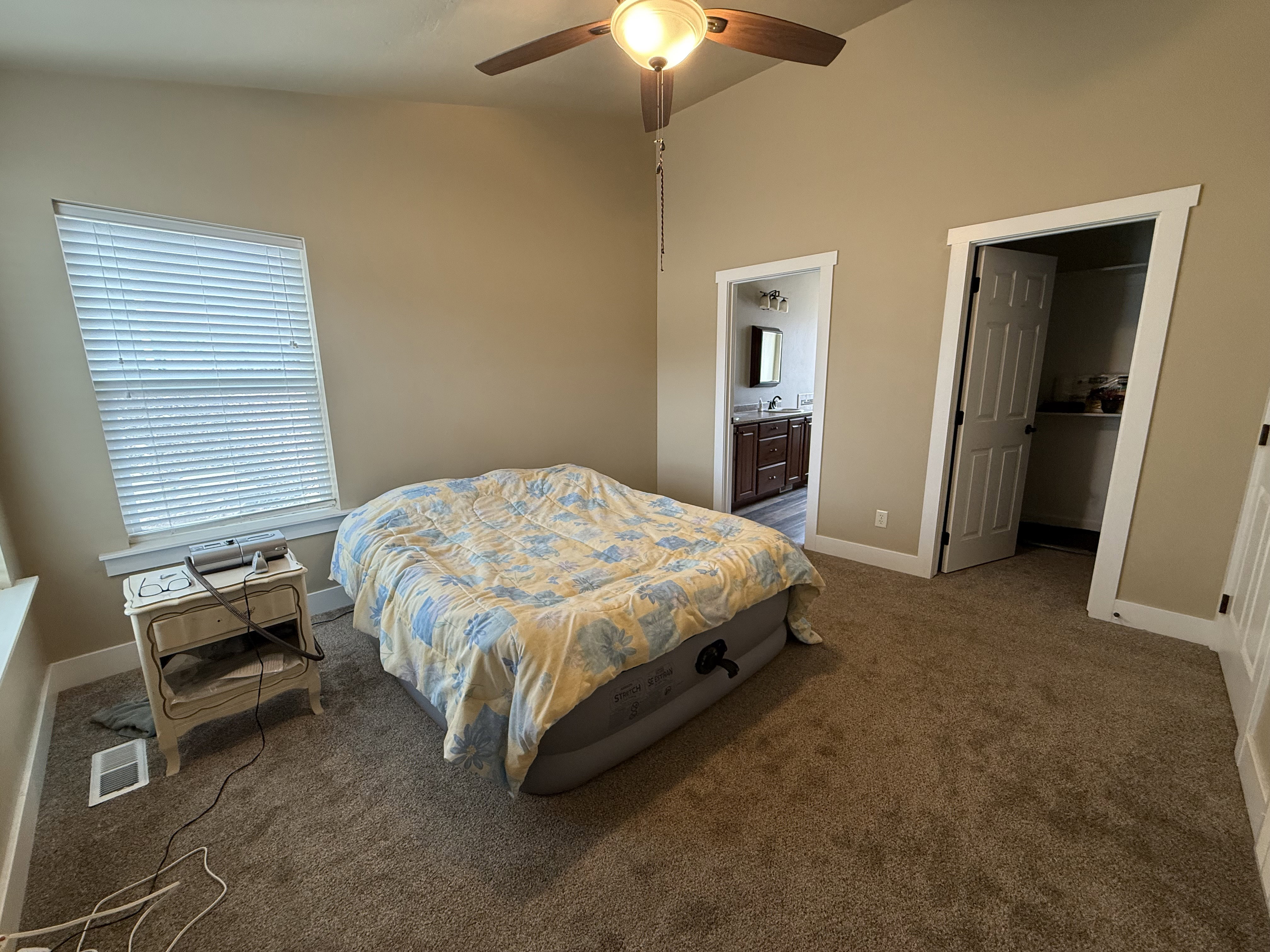 Carpeted bedroom with vaulted ceiling, connected bathroom, a ceiling fan, and a walk in closet