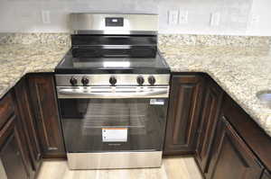 Kitchen with electric stove, dark wood finish cabinets, light stone counters, and light wood finished floors
