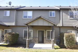 Rear view of property with a patio, stone siding, roof with shingles, and a yard