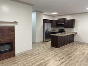 Kitchen featuring dark wood finish cabinetry, stainless steel appliances, a peninsula, crown molding, and a glass covered fireplace