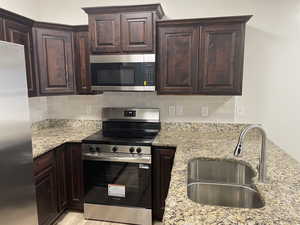 Kitchen with stainless steel appliances, dark wood finish cabinetry, backsplash, and light stone counters