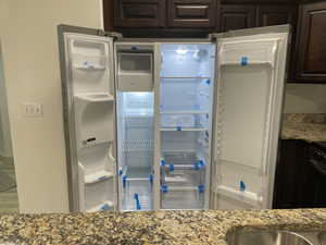 Kitchen view of dark wood finish cabinets, light stone counters, fridge, and tasteful backsplash