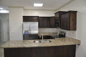 Kitchen with dark wood finish cabinets, stainless steel appliances, light stone counters, a peninsula, and crown molding