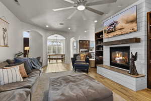 Living area with arched walkways, a glass covered fireplace, light wood-style flooring, recessed lighting, and a ceiling fan