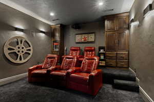 Cinema room with a textured wall, dark colored carpet, recessed lighting, and a textured ceiling