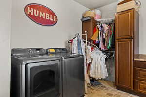 Laundry area with cabinet space, washer and clothes dryer, and light stone finish floors