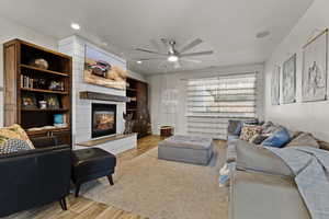 Living area featuring light wood-style floors, a large fireplace, a ceiling fan, recessed lighting, and a textured ceiling