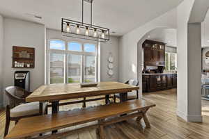 Dining room with arched walkways, light wood-type flooring, and a textured ceiling
