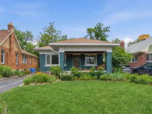 View of front facade with brick siding, a front yard, a chimney, and a shingled roof