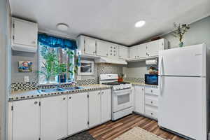 Kitchen featuring white appliances, light countertops, white cabinets, and tasteful backsplash