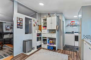 Kitchen featuring white cabinets, dark wood-style flooring, crown molding, lofted ceiling, and washing machine and dryer