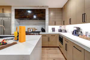 Kitchen featuring built in appliances, light wood finished floors, light stone counters, modern cabinets, and light wood finish cabinets