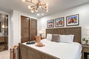 Bedroom featuring a closet, connected bathroom, a chandelier, and light colored carpet