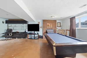 Rec room with finished concrete flooring, billiards, a fireplace, and a textured ceiling