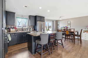 Kitchen featuring a kitchen island, freestanding refrigerator, backsplash, light countertops, and dark cabinets