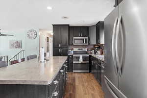 Kitchen with stainless steel appliances, dark cabinetry, dark wood-type flooring, light countertops, and a textured ceiling