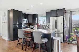 Kitchen featuring stainless steel appliances, a kitchen island, light countertops, light wood-type flooring, and a breakfast bar