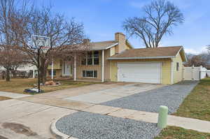 Bi-level home featuring driveway, a garage, a gate, brick siding, and a chimney