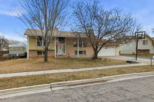 Raised ranch featuring brick siding, driveway, covered porch, a garage, and a front yard