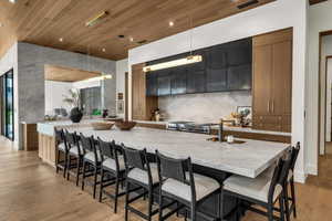 Kitchen featuring dual tone cabinets, decorative light fixtures, a breakfast bar area, wood ceiling, and stainless steel range with gas stovetop