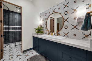 Bathroom with vanity, a tile shower, light tile patterned flooring, and decorative backsplash