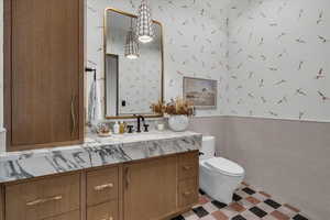 Half bath featuring wallpapered walls, a wainscoted wall, vanity, tile walls, and light flooring