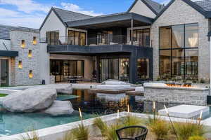Back of house featuring a balcony, a patio area, stone siding, and a swimming pool