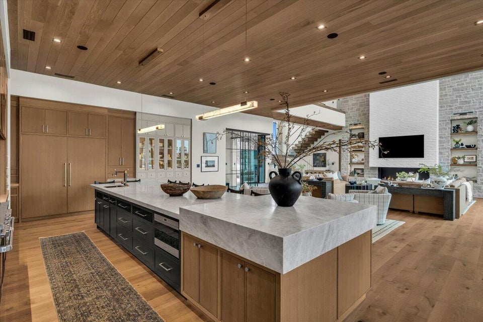 Two tone kitchen with wooden ceiling, a large island with sink, light wood-style floors, open floor plan, and light stone countertops