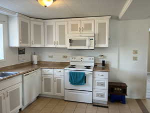 Kitchen with white appliances, white cabinets, light tile patterned floors, and light countertops