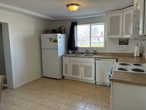 Kitchen with white cabinets, white appliances, ornamental molding, and light countertops