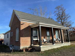 Front view of property with brick siding, covered porch, and a shingled roof