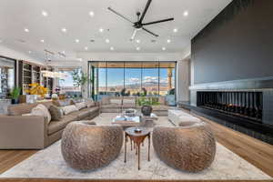 Living room with light wood-type flooring, a tiled fireplace, a mountain view, ceiling fan, and suspended lighting