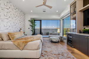 Bedroom with an accent wall, wallpapered walls, light wood-type flooring, beverage cooler, and ceiling fan