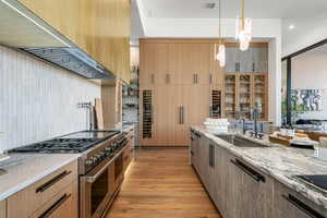 Kitchen with light stone counters, ventilation hood, double oven range, modern cabinets, and decorative light fixtures